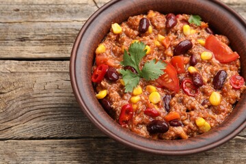 Tasty chili con carne in bowl on wooden table, closeup. Space for text