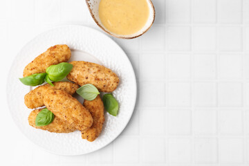 Tasty fried croquettes, basil and sauce on white tiled table, top view. Space for text
