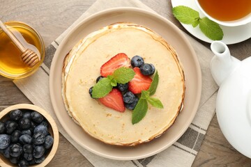 Delicious crepes with berries, cream, mint, honey and tea on wooden table, flat lay