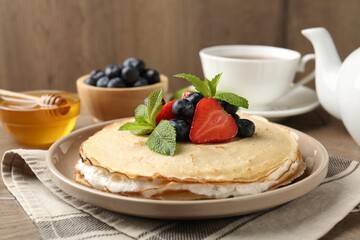 Delicious crepes with berries, cream, mint, honey and tea on wooden table, closeup