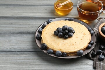 Delicious crepes with blueberries, honey and tea on grey wooden table, closeup. Space for text