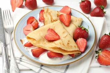 Delicious crepes with strawberries and cream on table, closeup
