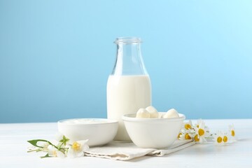 Fresh dairy products and flowers on white wooden table against light blue background