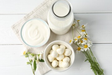 Fresh dairy products and flowers on white wooden table, flat lay