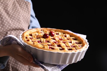 Woman holding tasty cherry pie on black background, closeup