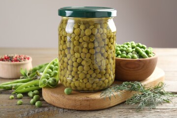 Pickled peas in jar, spices, dill and pods on wooden table, closeup