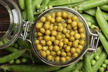 Pickled peas in jar and pods on wooden table, flat lay