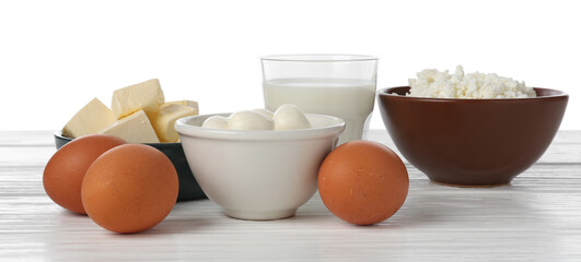 Different dairy products and eggs on wooden table against white background