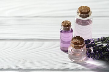 Natural essential oil and lavender flowers on white wooden table, closeup. Space for text