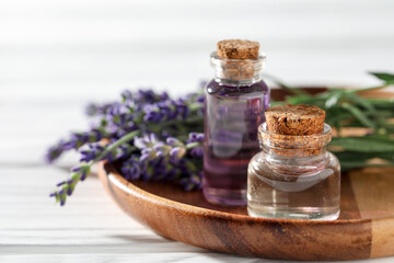 Natural essential oil and lavender flowers on white wooden table, closeup