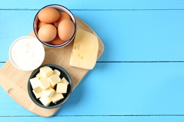 Different dairy products and eggs on light blue wooden table, flat lay. Space for text