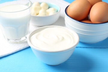 Different dairy products and eggs on light blue wooden table, closeup