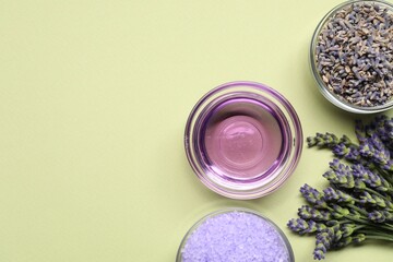 Natural essential oil, sea salt and lavender flowers on light green background, flat lay. Space for...