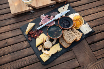 Gourmet appetizer plate with cheese, cold cuts, bread, jam, dried fruit and dehydrated mushrooms on a slate plate on a wooden table