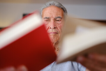 Elderly man holding two books and choosing one thoughtfully