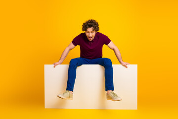 Young man sitting against vibrant yellow background presenting a playful expression and casual...