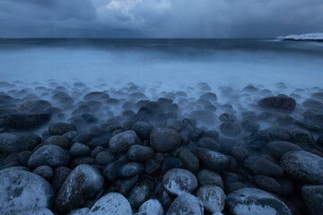 Tranquil coastal scene featuring smooth stones and misty waves under a cloudy sky, capturing the essence of nature's calm and beauty