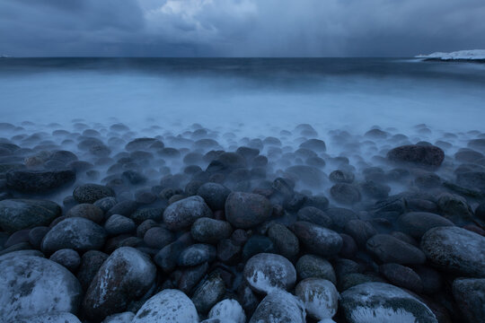 Tranquil coastal scene featuring smooth stones and misty waves under a cloudy sky, capturing the essence of nature's calm and beauty