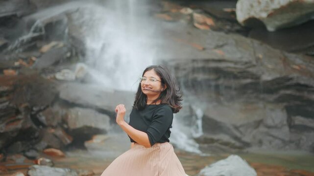 4K Portrait of Indian woman at beautiful waterfall in Sural Bhatori, Pangi Valley, India. Tourist exploring hidden gems in mountains. Woman enjoying tranquility by a waterfall. Travel and holidays 
