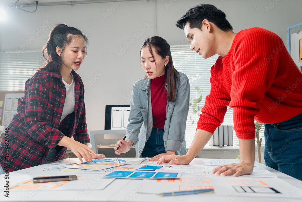 Poster asian ux designers collaborating on mobile app interface wireframe design in a modern office, engagi