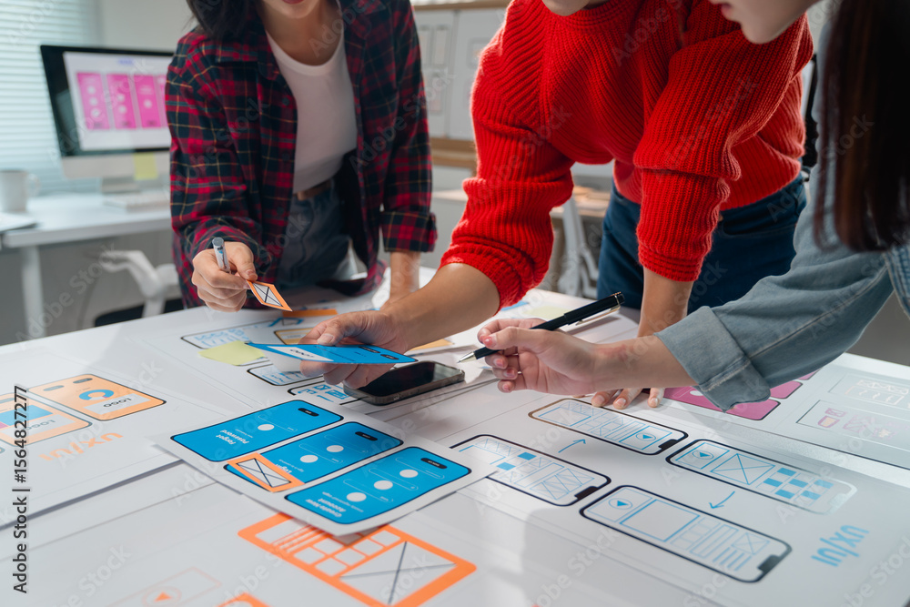 Poster three asian ux designers are discussing and improving the design of a mobile application during a wo