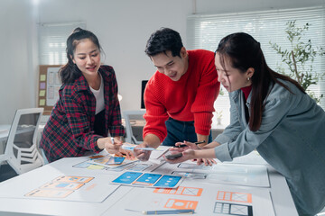 Asian UX designers collaborating on a wireframe for a mobile application, comparing their designs...