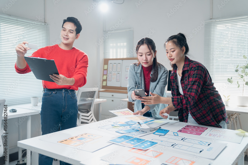 Poster group of young asian ui/ux developer team working and discussing mobile app interface wireframe desi