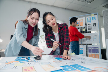 Two young female UX designers collaborating on mobile app user interface and experience, comparing...