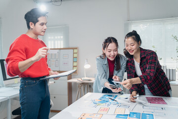 Young asian ux web designers working and designing mobile app interface wireframe design together...
