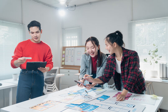 Diverse team of young professionals engaging in a collaborative brainstorming session for mobile app design. They are discussing ideas and reviewing wireframe layouts in a modern office - Powered by Adobe