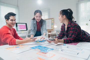 Three young professionals engaging in a collaborative discussion while designing a mobile app interface. They are surrounded by colorful wireframes and digital design tools in a bright office
