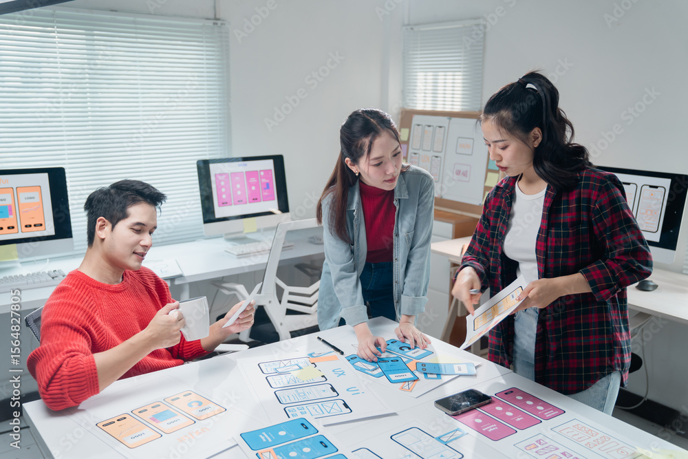 Poster asian ui/ux designers collaborating on mobile app interface wireframe design while working together 