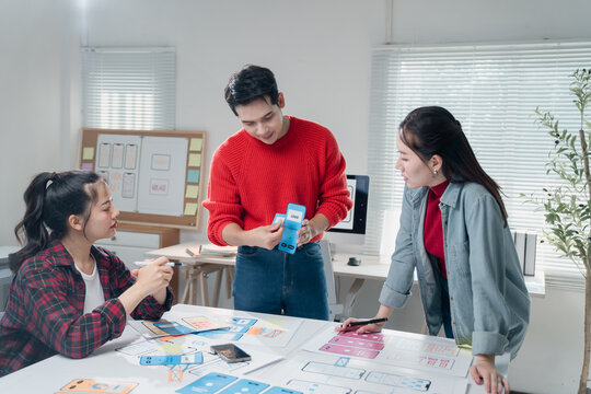 Young asian ux ui designers working on smartphone interface wireframe design collaborating on mobile app layout prototype development in the office