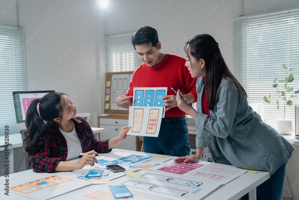 Poster creative team discussing and developing a mobile app interface. designers examine wireframes and pro