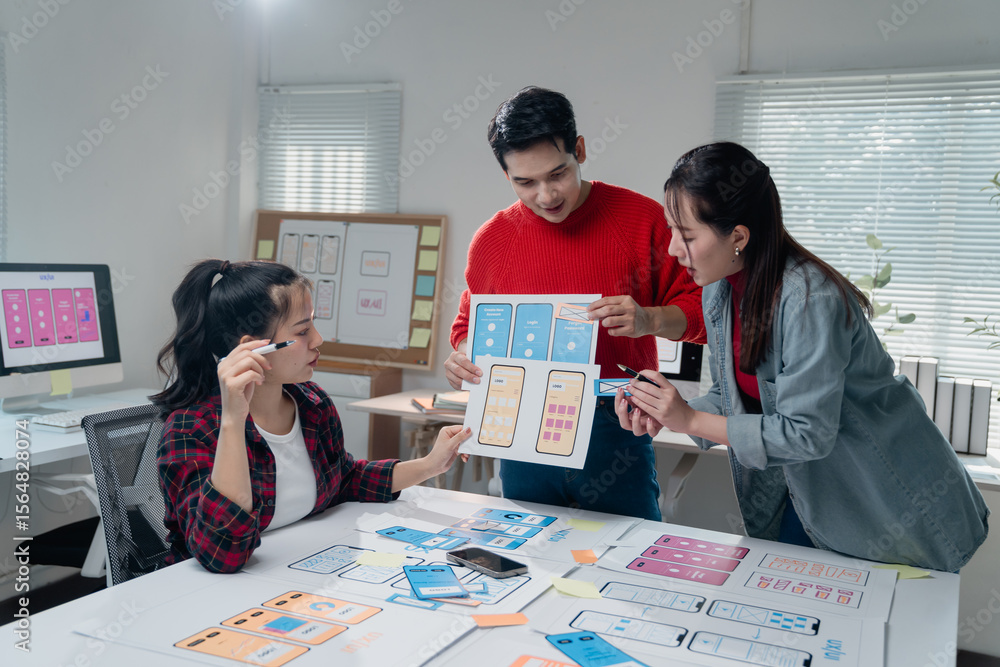 Poster three asian ux designers working together in a modern office, analyzing and discussing mobile app in