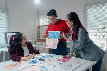 Creative team discussing and developing a mobile app interface. Designers examine wireframes and...