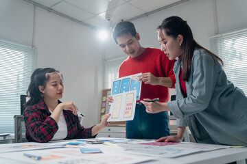 Three Asian user experience designers are collaborating on a new mobile app interface wireframe...