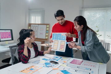 Three Asian ux designers working together in a modern office, analyzing and discussing mobile app...