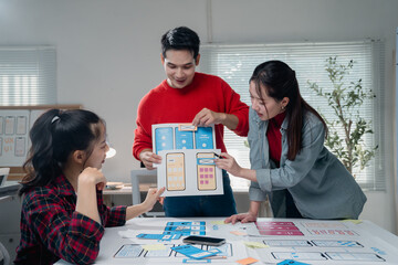 Young asian ux graphic designers team working together on mobile application interface wireframe design, discussing smartphone user interface design at modern workplace