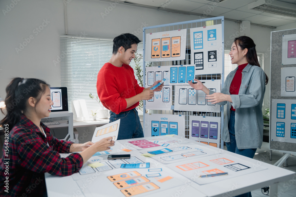 Poster creative team engaged in designing a mobile app interface, discussing layouts and features. diverse 