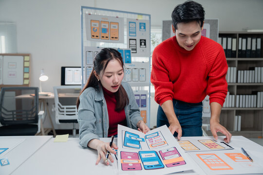 Two young asian ui/ux web designers are working together developing mobile app design at modern office, discussing user interface layouts for mobile apps - Powered by Adobe