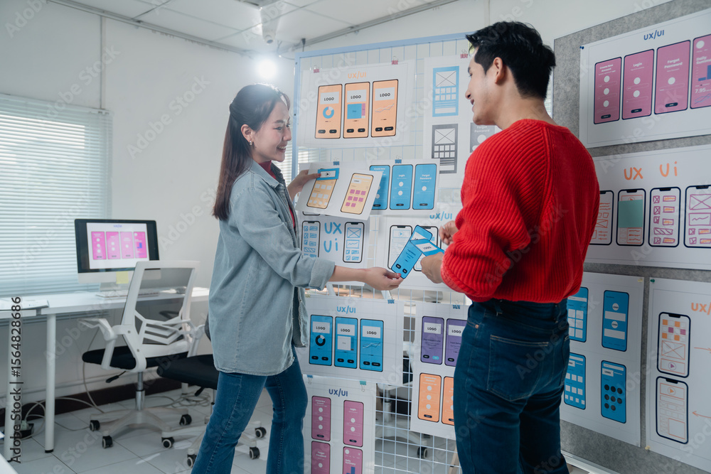 Poster two designers collaborate on mobile app interface designs, examining wireframes and prototypes on a 