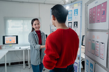 Two asian web designers shaking hands after designing user interface for mobile application in...