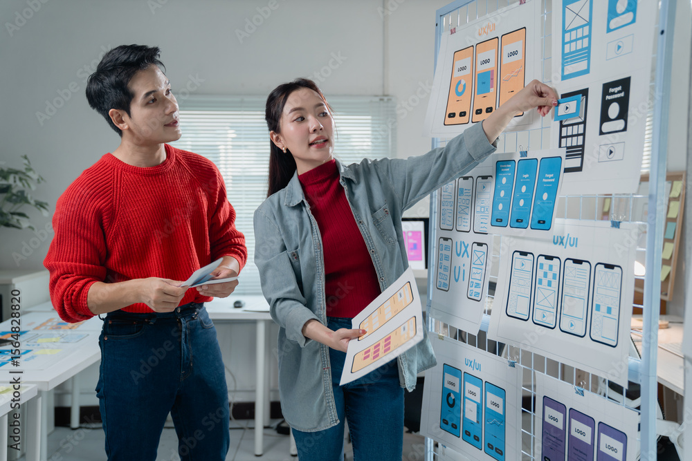 Poster two young asian designers working together in the office, evaluating ux/ui design of mobile app inte