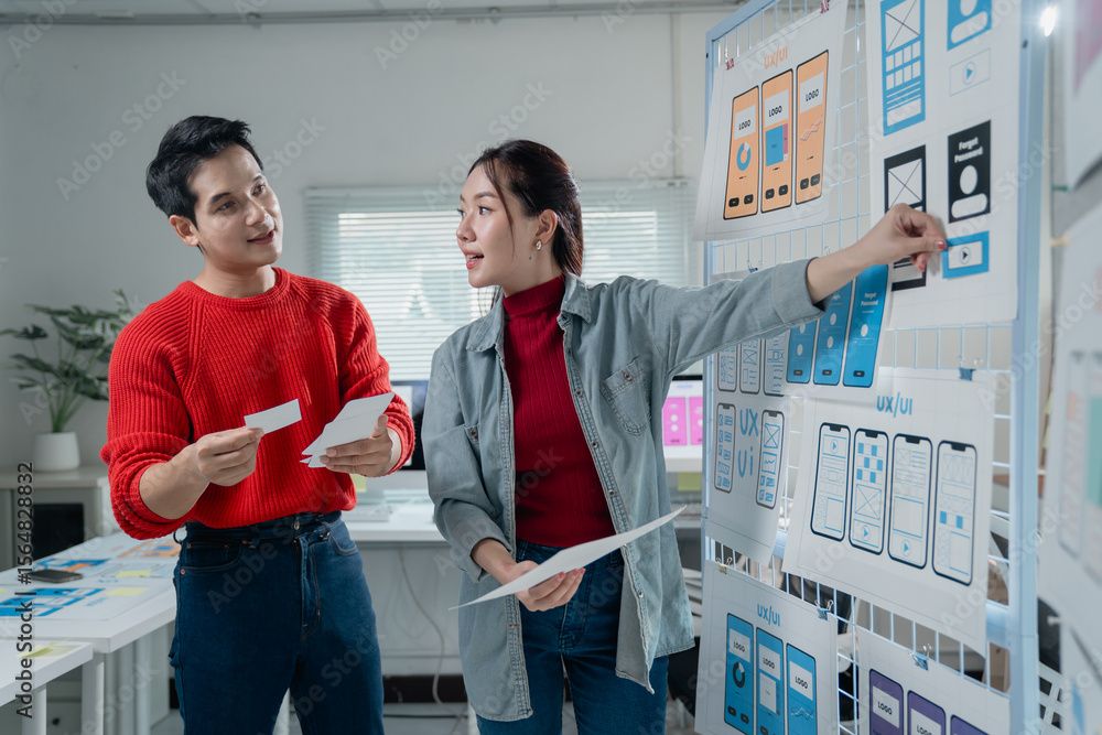 Poster two young asian ux/ui designers discussing and working on a new mobile application prototype in thei