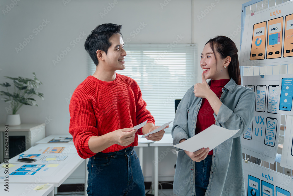 Poster two asian ux/ui designers engaging in a collaborative discussion about mobile app interface wirefram