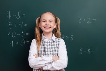 Smiling young schoolgirl in front of chalkboard demonstrating academic skills and confidence during...
