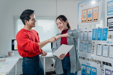 Two asian colleagues fist bumping after finishing designing new mobile app screens, which are...