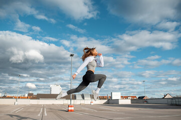 Woman Leaping on Rooftop Against Cloudy Sky