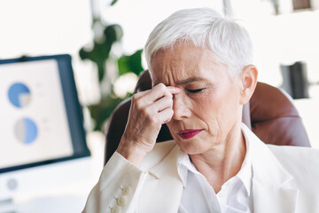 Mature businesswoman with short white hair looking stressed while sitting in an office environment...